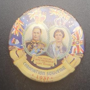 Puede incluir: Un botón redondo y colorido con una imagen del rey Jorge VI y la reina Isabel en sus túnicas de coronación. El botón tiene el texto "Coronation Souvenir 1937" y una representación de fuegos artificiales.