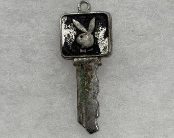May include: A silver key charm with a black square charm featuring a white bunny rabbit with a bow tie.