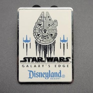 May include: A silver pin with a white background featuring a Star Wars: Galaxy's Edge logo, a depiction of the Millennium Falcon, and the Disneyland Resort logo.