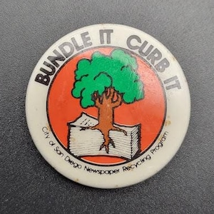Könnte beinhalten: Weißer Knopf mit einem grünen Baum und einem Stapel Zeitungen. Der Knopf lautet "Bundle It Curb It City of San Diego Newspaper Recycling Program".