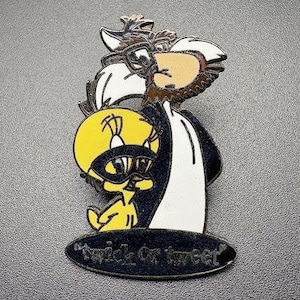 Op de afbeelding: Een zwart-witte emaille pin met Tweety Bird en Sylvester de Kat in kostuums. Tweety draagt ​​een zwart masker en Sylvester draagt ​​een witte robe. De pin heeft de tekst "Trick or Tweet" onderaan.