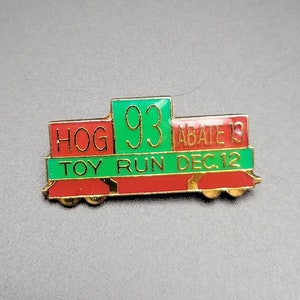 May include: A red, green, and gold metal pin shaped like a train with the text "HOG 93 ABATE 19 TOY RUN DEC. 12"
