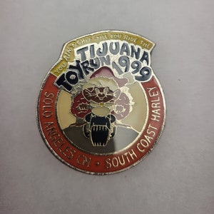 May include: A red, white, and yellow enamel pin with a cartoon Santa Claus riding a motorcycle. The pin says "You ain't chit till you ride the Tijuana Toy Run 1999 Solo Angeles CM. South Coast Harley."