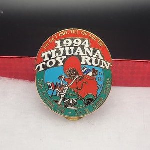 May include: A red, white, and blue enamel pin with a cartoon character riding a motorcycle. The pin says "You ain't chit, till you ride the 1994 Tijuana Toy Run, Los Angeles CM - South Coast Harley".