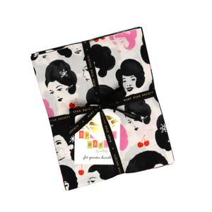 Op de afbeelding: Een stoffen fat quarter bundel vastgebonden met een zwart lint bedrukt met de tekst Ruby Star Society. De stof heeft een witte achtergrond met een herhalend patroon van zwarte en roze gestileerde gezichten en rode kersen. Een wit label vermeldt Sparkle Mart.