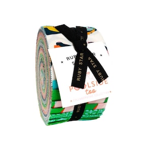 Pode incluir: Um rolo de tiras de tecido coloridas, amarrado com uma fita preta e uma etiqueta. O tecido apresenta vários padrões e cores, incluindo verde, rosa e azul. A etiqueta diz "RUBY STAR POOLSIDE too COLLABORATIVE COLLECTION."