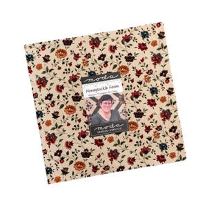 May include: A square piece of cream-colored fabric featuring a repeating floral pattern in shades of red, dark blue, and orange. A rectangular label is attached to the center, displaying the text "moda", "Honeysuckle Farm", and "Kansas Troubles Quilters".