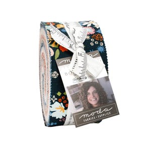 May include: A rolled bundle of fabric with a dark blue floral design, incorporating orange, pink, and white elements. It's secured with a white ribbon and a tag displaying a woman's image and the text "moda FABRICS + SUPPLIES".