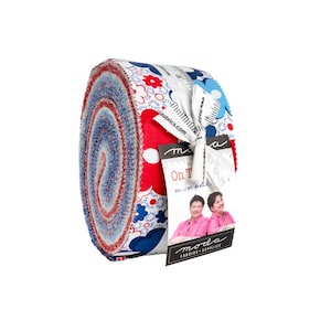 May include: A rolled bundle of fabric strips featuring a red, white, and blue floral and geometric pattern. A white paper tag is tied around the roll with a ribbon, displaying the text On The and featuring a photograph of two people.