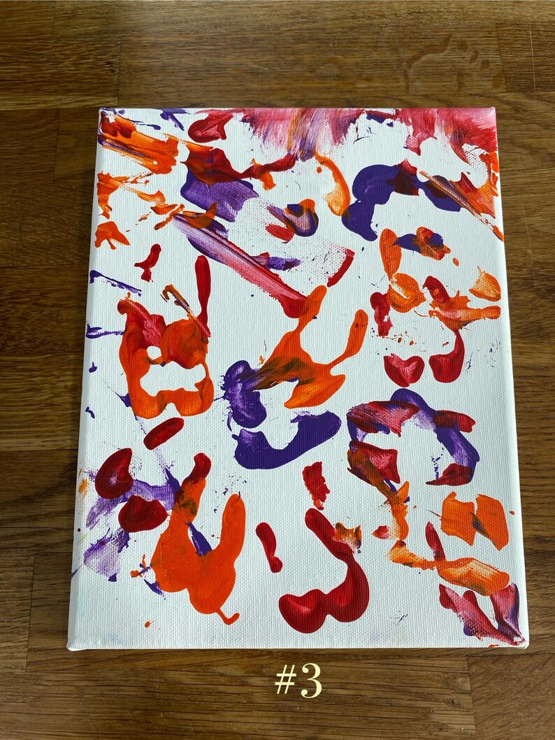 Op de afbeelding: Abstract canvas kunstwerk met een witte achtergrond en levendige spatten van rode, oranje en paarse verf. Het kunstwerk toont een verscheidenheid aan penseelstreken en spetters, met het nummer "#3" in goud aan de onderkant.