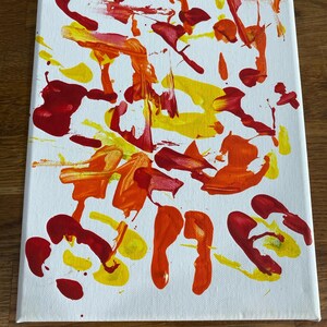 Op de afbeelding: Abstract schilderij op een wit canvas met gedurfde streken van rode, gele en oranje verf. Het kunstwerk toont een verscheidenheid aan vormen en texturen, met het nummer "#1" in zwart onderaan.