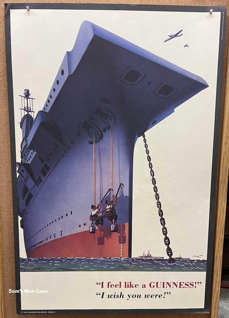 Op de afbeelding: Vintage Guinness-advertentieposter met een groot schip en de tekst "I feel like a GUINNESS!" en "I wish you were!". De poster heeft een blauw en rood kleurenschema met een ketting en twee kleine vliegtuigen.