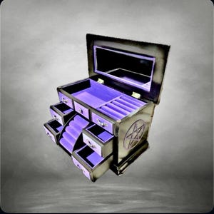 Puede incluir: Caja de joyería negra con un diseño de pentagrama en el lateral. La caja tiene múltiples cajones y compartimentos forrados con terciopelo morado. Un espejo está dentro de la tapa.