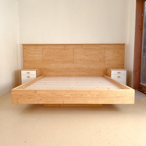 Peut inclure: Un cadre de lit en bois clair avec une tête de lit et deux tables de chevet blanches. Le cadre de lit est en bois clair et présente un design simple et moderne. La tête de lit est composée de plusieurs panneaux de bois.