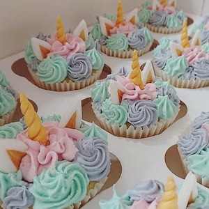 May include: A tray of unicorn cupcakes decorated with pastel pink, blue, and purple frosting. Each cupcake has a white unicorn horn with a gold tip.