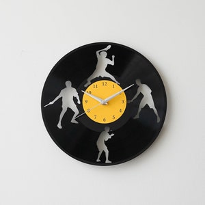 Könnte beinhalten: Eine schwarze Schallplattenuhr mit gelbem Zentrum und weißen Zeigern. Die Uhr zeigt vier Silhouetten von Personen, die Sport treiben, darunter Tennis, Basketball und Fußball.