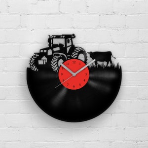 Op de afbeelding: Zwarte vinyl platen klok met een silhouet van een tractor en een koe in een veld. De wijzerplaat van de klok heeft rode cijfers en een zilveren wijzer.