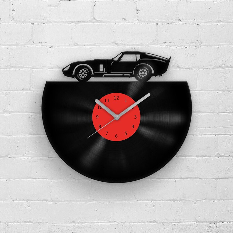 May include: A black vinyl record clock with a silver hand and red numbers. A black silhouette of a sports car is on top of the clock.