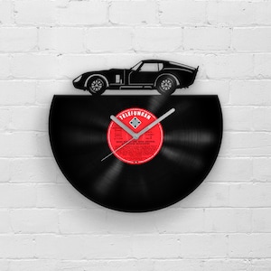 May include: A black vinyl record clock with a silver clock hand and a black silhouette of a car on top. The record label is red and says "Telefunken" and "Fritz Muenchow und Seine Original Dresdner Mozartanten".