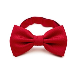 May include: A red bow tie made from textured fabric. The bow tie is tied and ready to wear.