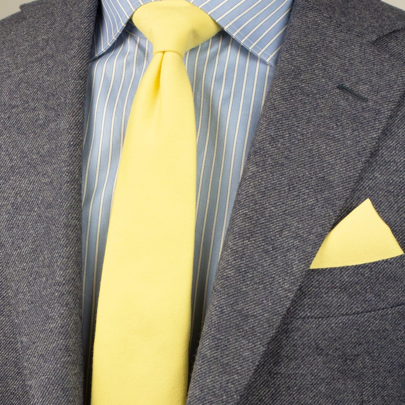 May include: A gray blazer with a yellow tie and a yellow pocket square. The shirt is light blue with white stripes.