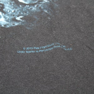 May include: A black t-shirt with a blue and white graphic print. The text "&copy; 2015 Pink Floyd Music Ltd. Under license to Peryscope Productions, Inc. LLC" is printed on the bottom of the shirt.
