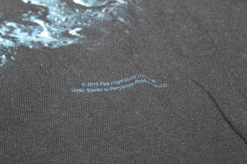 May include: A black t-shirt with a blue and white graphic print. The text "&copy; 2015 Pink Floyd Music Ltd. Under license to Peryscope Productions, Inc. LLC" is printed on the bottom of the shirt.