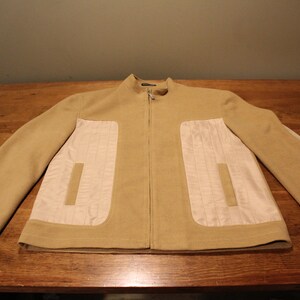 May include: A tan zip-up jacket with a white quilted panel on each side. The jacket has a stand-up collar and long sleeves.