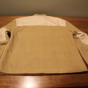 May include: A tan jacket with white elbow patches and a white panel across the back.