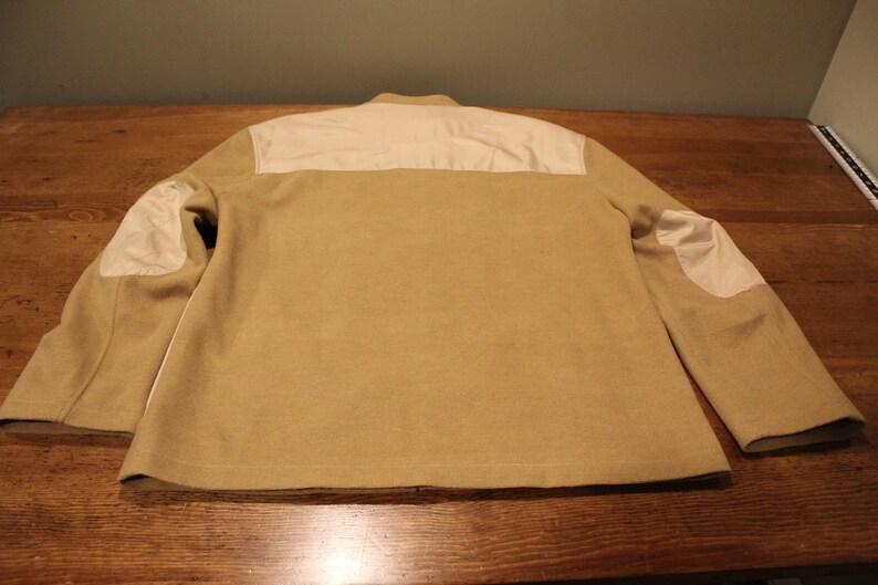 May include: A tan jacket with white elbow patches and a white panel across the back.