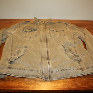 May include: A brown canvas jacket with a zipper closure and multiple pockets. The jacket has a stand-up collar and long sleeves.