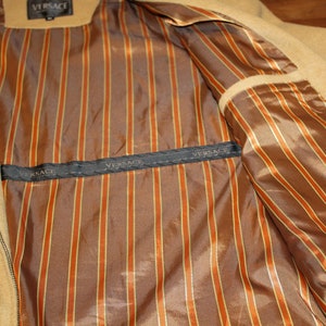 May include: The inside of a tan jacket with a brown and orange striped lining. The lining has the word "VERSACE" printed on it.
