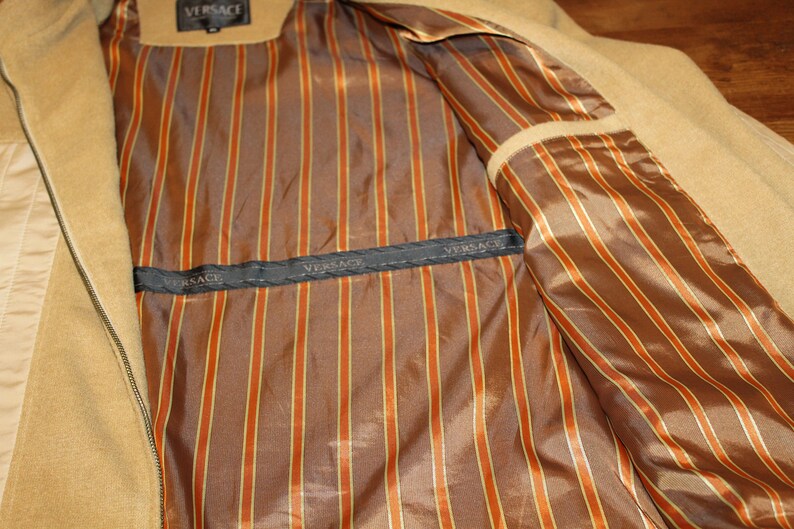 May include: The inside of a tan jacket with a brown and orange striped lining. The lining has the word "VERSACE" printed on it.
