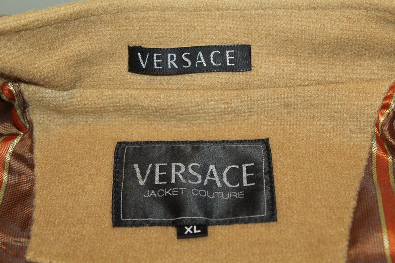 May include: Black label with white text reading "VERSACE JACKET COUTURE" and "XL" on a brown fabric background.