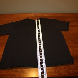 May include: Black t-shirt laid flat on a wooden surface with a measuring tape showing a length of 68.58 cm.