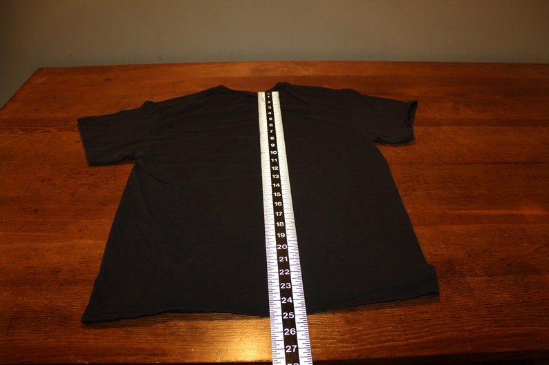 May include: Black t-shirt laid flat on a wooden surface with a measuring tape showing a length of 68.58 cm.