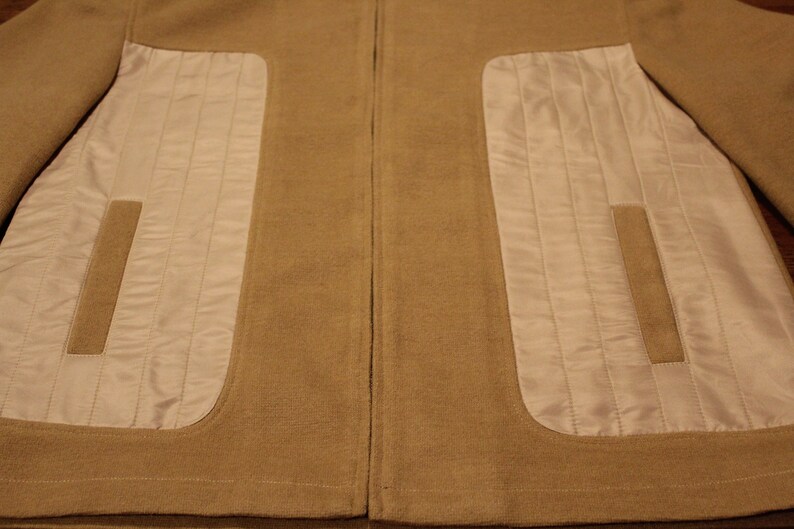 May include: A brown jacket with a zipper closure and two white quilted panels on the front.