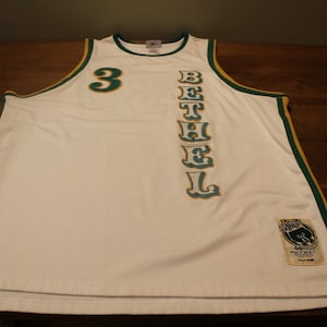 May include: White basketball jersey with green and gold trim. The number "3" is on the front of the jersey, and the word "BETHEL" is vertically down the right side. A small patch with a bear logo is on the bottom right side of the jersey.