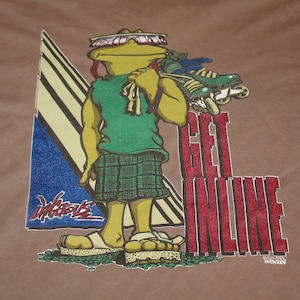 May include: A brown t-shirt with a cartoon frog wearing green shorts and holding inline skates. The text "Get Inline" is printed in red on the shirt.