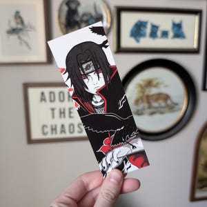May include: A bookmark featuring a black and red anime character illustration. The character has black hair and red eyes, with a black and red outfit. The bookmark has the text "ADORE THE CHAOS".