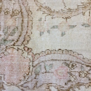May include: Close-up of a cream-colored rug with a floral pattern in shades of brown, pink, and green. The rug has a fringed edge.