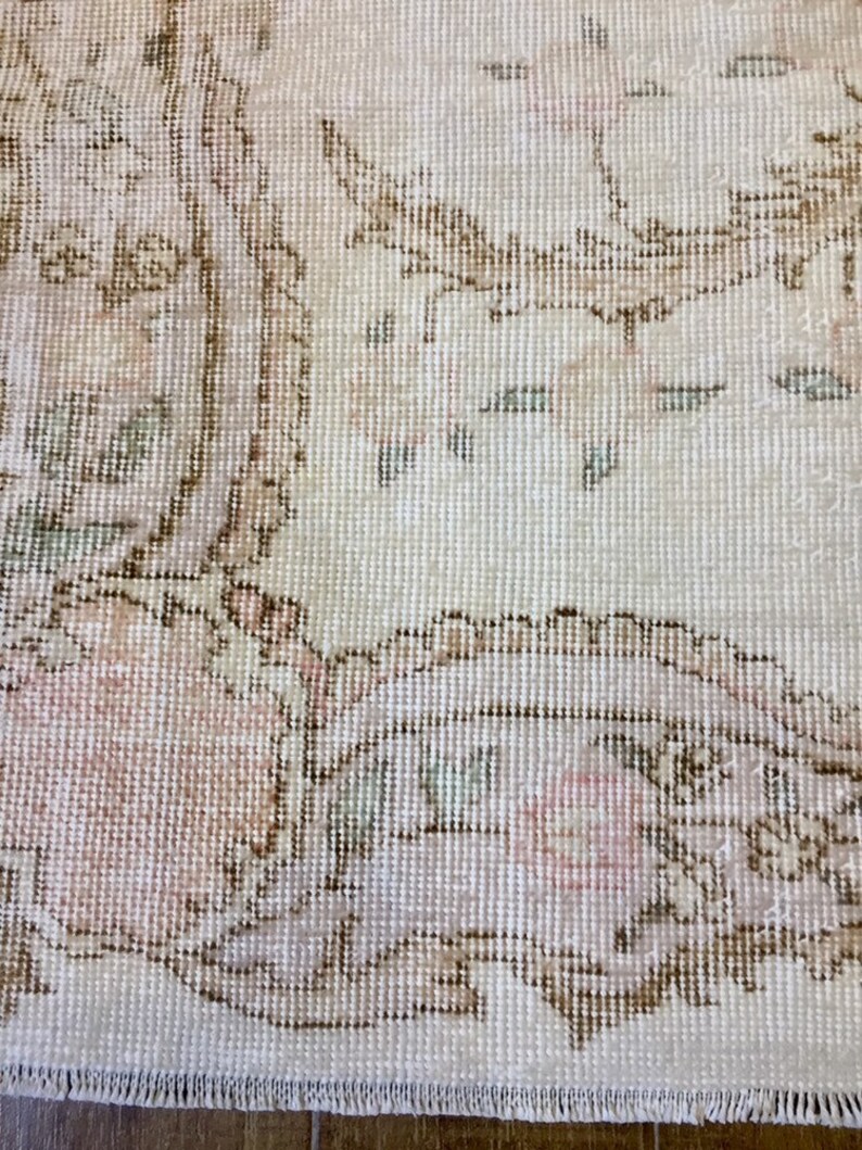 May include: Close-up of a cream-colored rug with a floral pattern in shades of brown, pink, and green. The rug has a fringed edge.