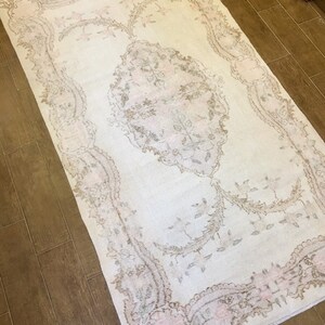 May include: A white rug with a delicate floral pattern in shades of beige and pink. The rug has a distressed look, giving it a vintage feel.