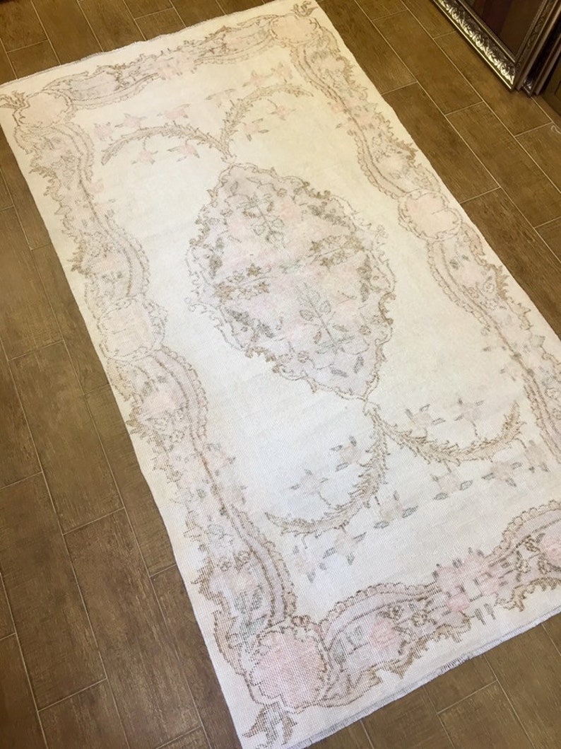 May include: A white rug with a delicate floral pattern in shades of beige and pink. The rug has a distressed look, giving it a vintage feel.