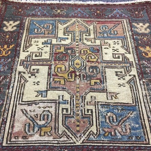 May include: A vintage rug with a geometric pattern in shades of blue, red, yellow, and white. The rug has a dark grey border with intricate designs.