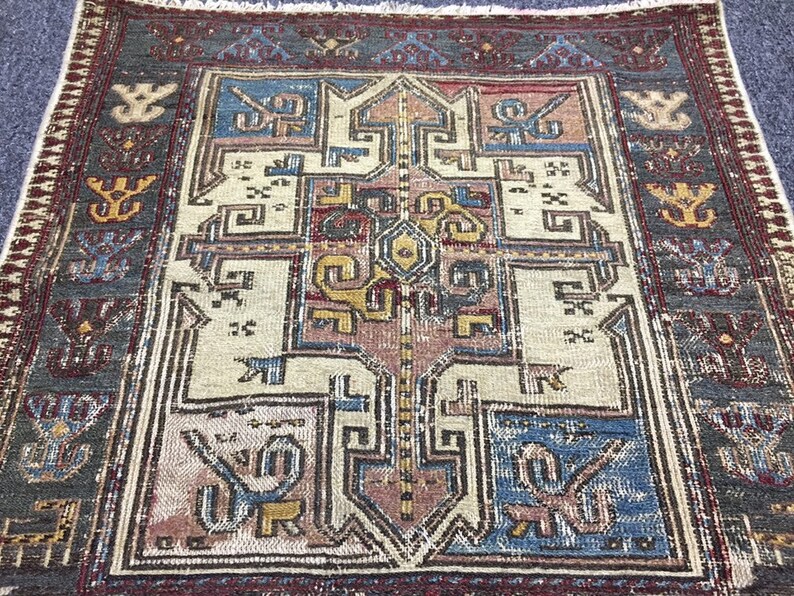 May include: A vintage rug with a geometric pattern in shades of blue, red, yellow, and white. The rug has a dark grey border with intricate designs.