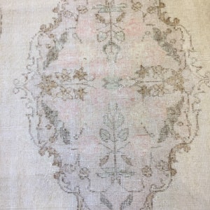 May include: A vintage rug with a delicate floral pattern in shades of brown and beige. The rug has a distressed look, with faded colors and a worn texture.