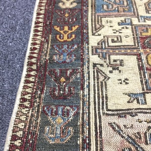 May include: Close-up of a rug with a geometric pattern in shades of blue, red, and beige. The rug has a fringed border.