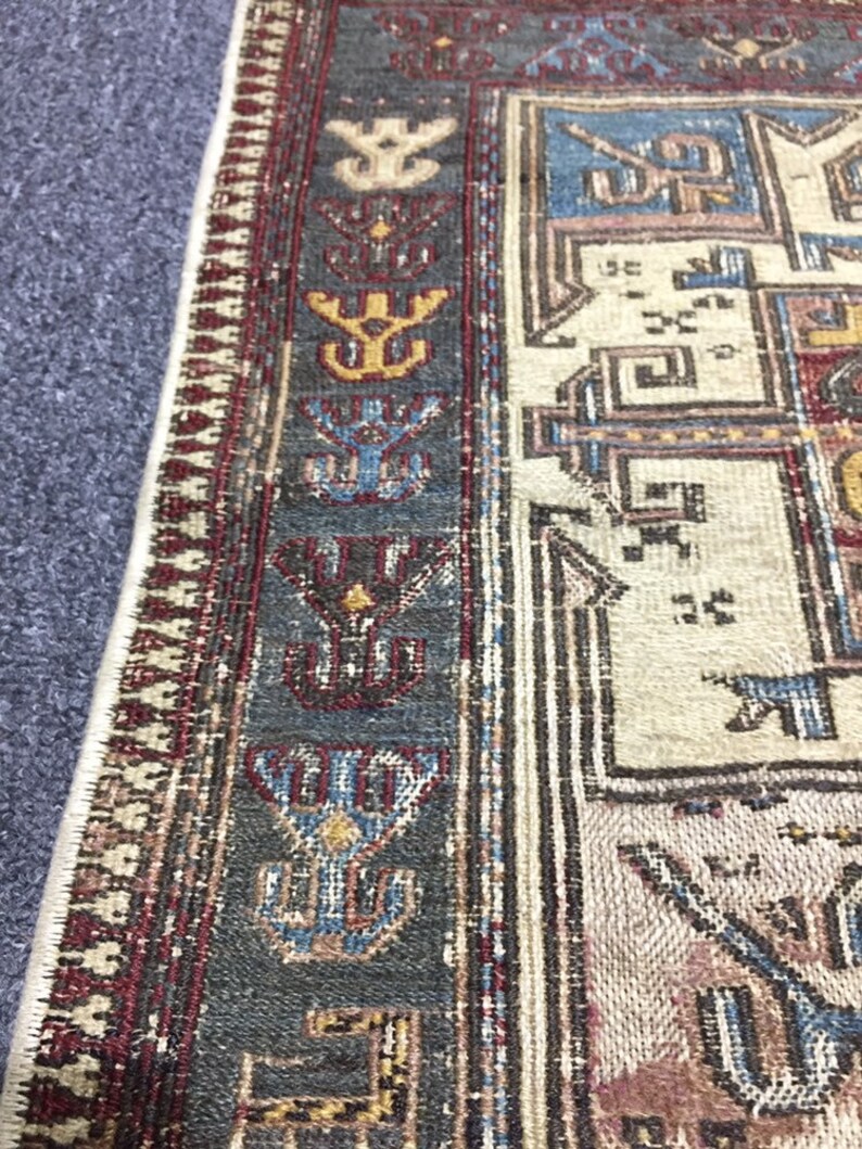 May include: Close-up of a rug with a geometric pattern in shades of blue, red, and beige. The rug has a fringed border.