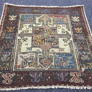 Puede incluir: Una alfombra vintage con un patrón geométrico en tonos rojos, azules, amarillos y blancos. La alfombra tiene un borde con flecos y está hecha de lana.